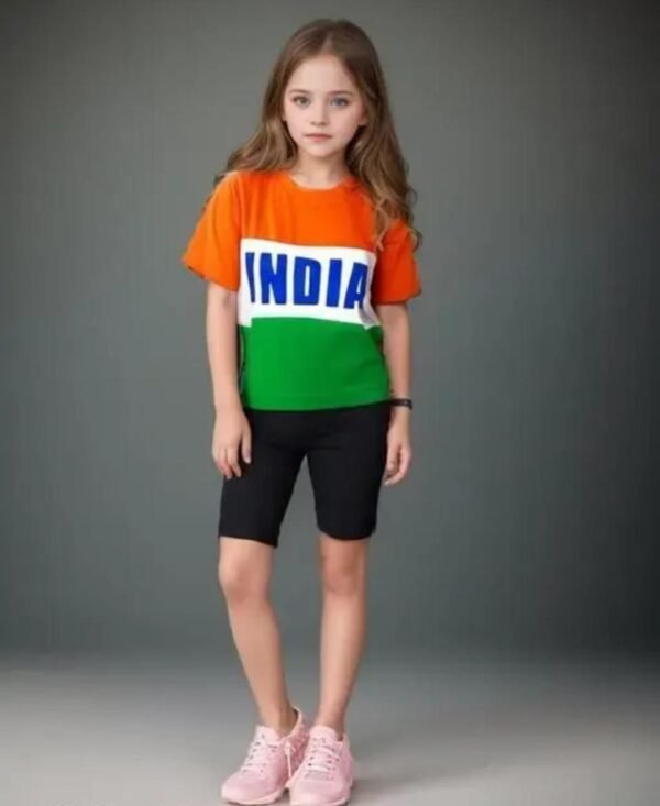 Child wearing a t-shirt with orange, white, and green stripes and “INDIA” written in blue, paired with black shorts and pink sneakers, standing against a plain background