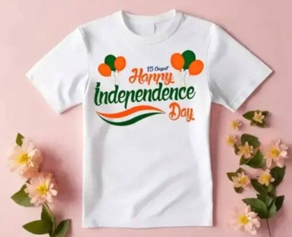 White kids’ T-shirt with “15 August Happy Independence Day” text in green and orange, three balloons, and a wavy tricolor flag design, placed on a pink background with flowers